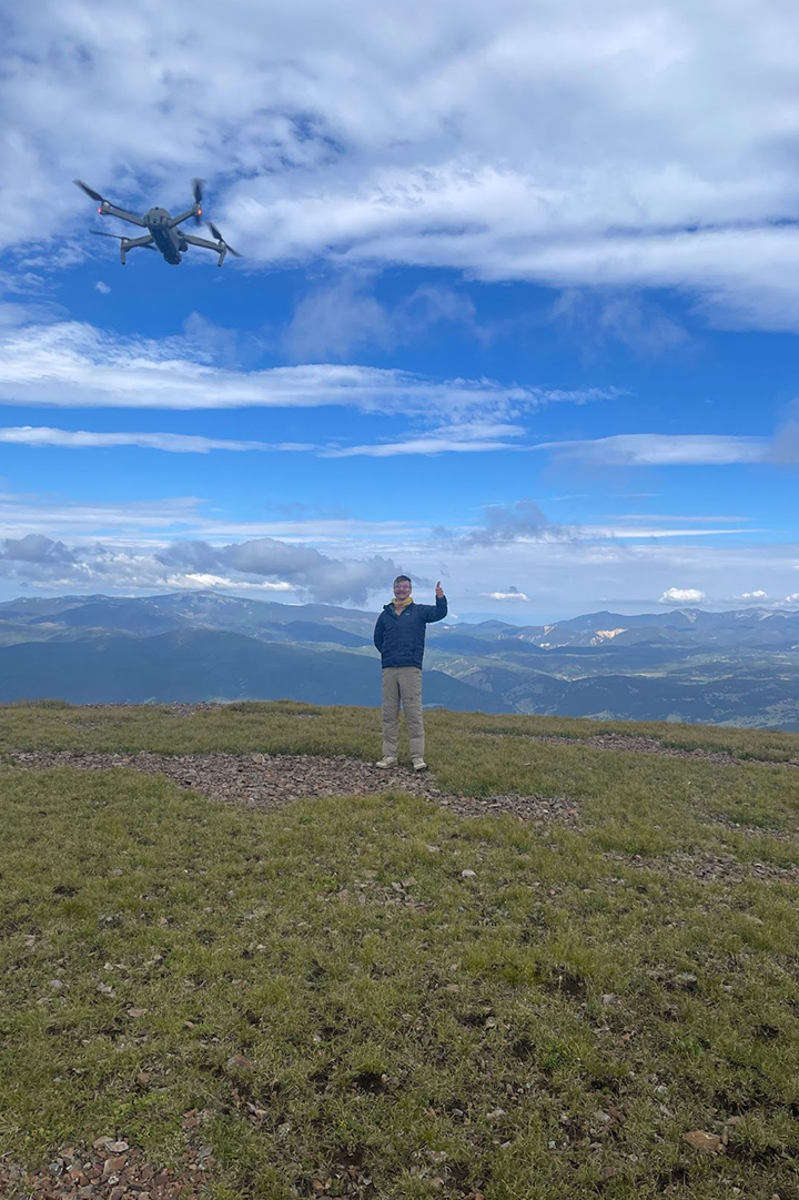 John Lesko flies a drone in a grassy field with a blue sky overhead