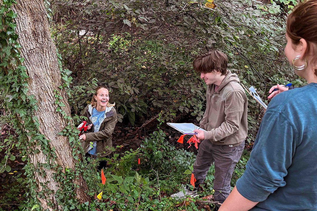 Three geography students in the woods holding papers and taking measurements