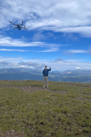 John Lesko flies a drone in a grassy field with a blue sky overhead