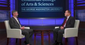 Dmitry Streletskiy and Dean Paul Wahlbeck seated on a stage talking with a Columbian College of Arts and Sciences logo
